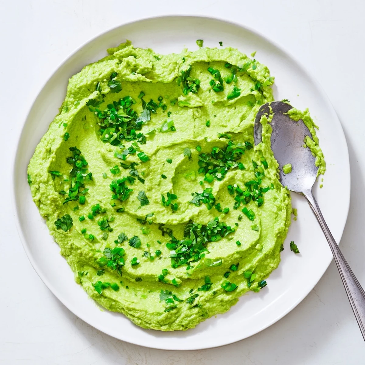 A close-up of vibrant avocado lime dip in a rustic serving bowl, surrounded by colorful vegetable sticks and fresh lime wedges.  