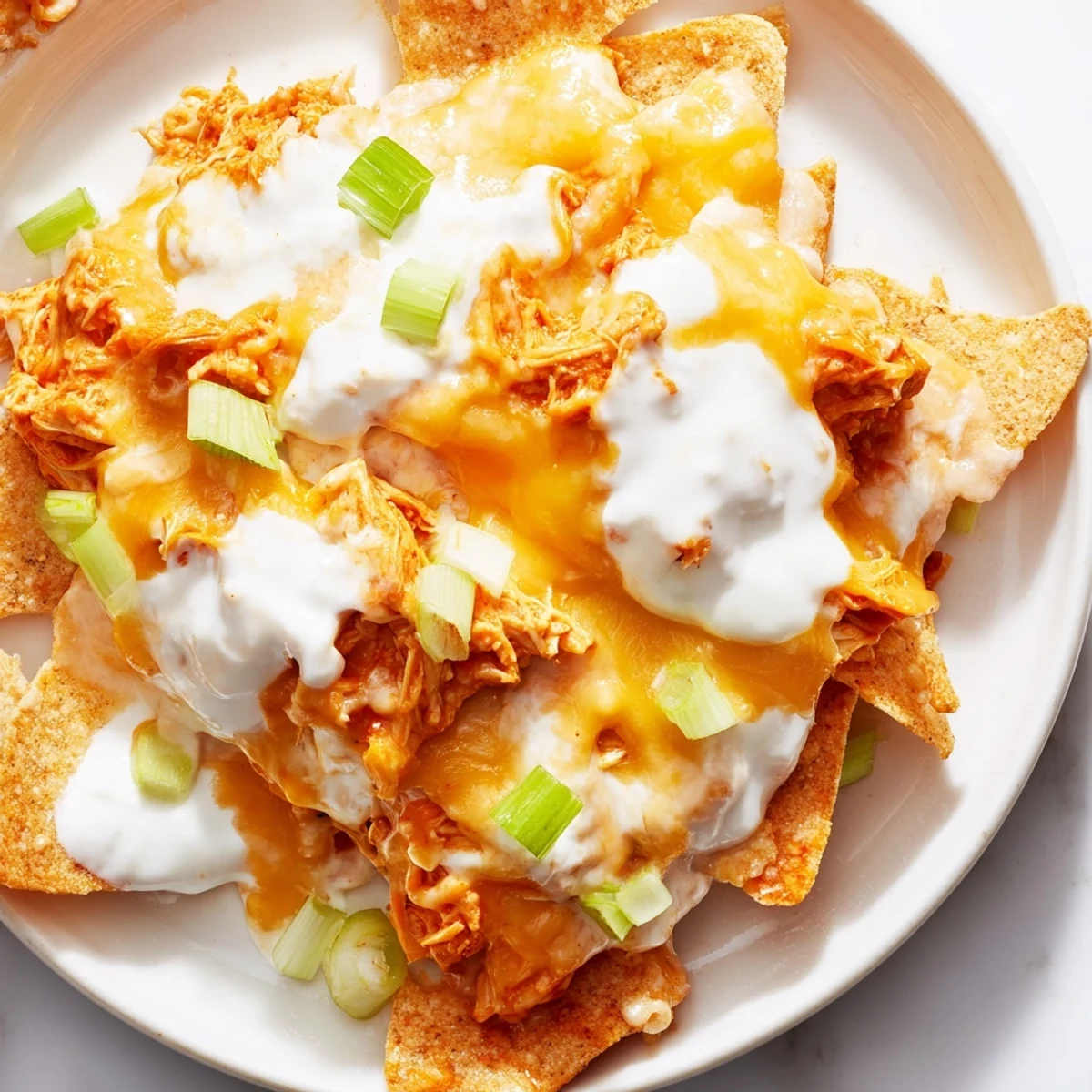 A close-up of Buffalo Chicken Nachos with melted cheddar and Monterey Jack cheese over spicy shredded chicken and crispy tortilla chips.