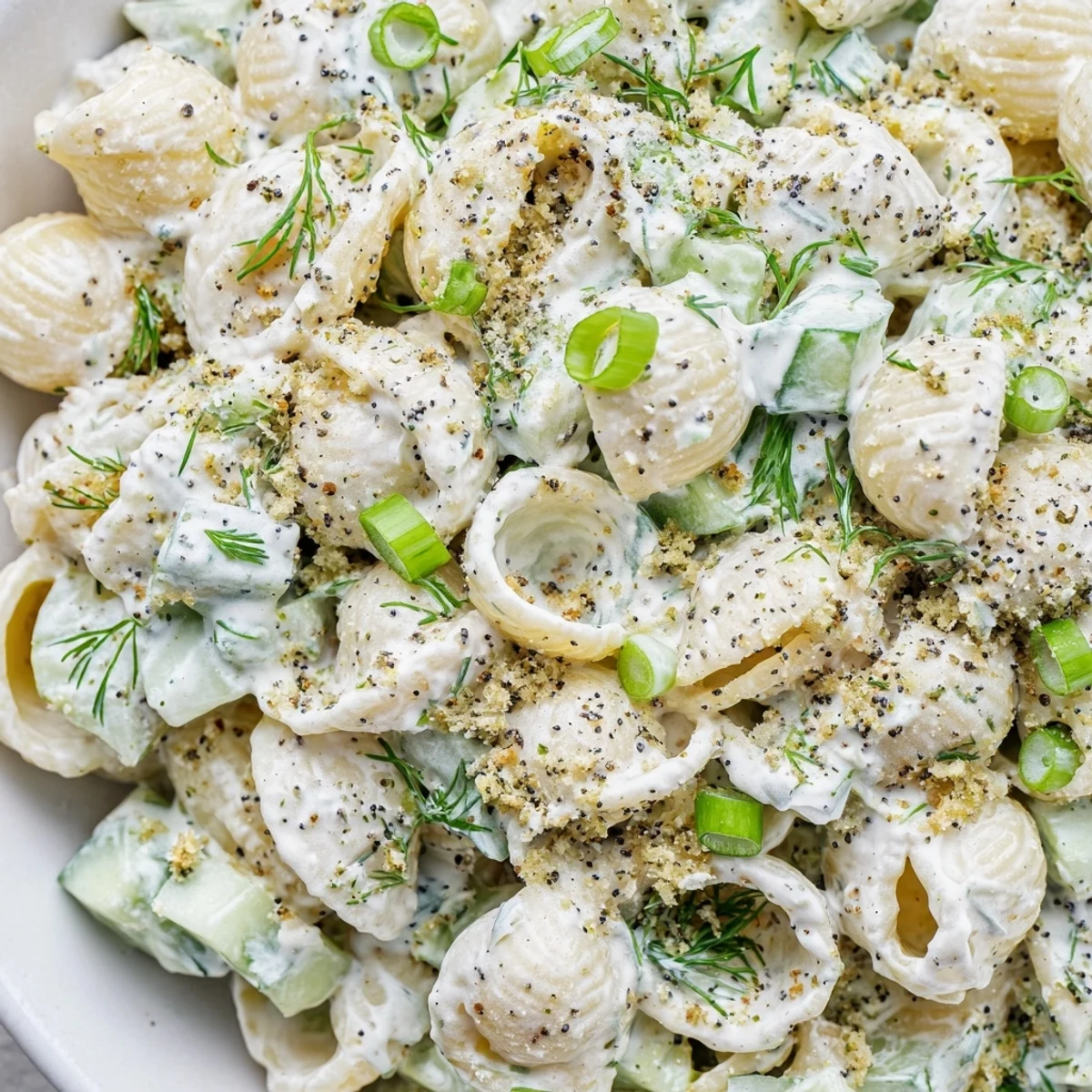 Crisp diced cucumber and tender shell pasta tossed with creamy dressing and fresh dill in a serving bowl.