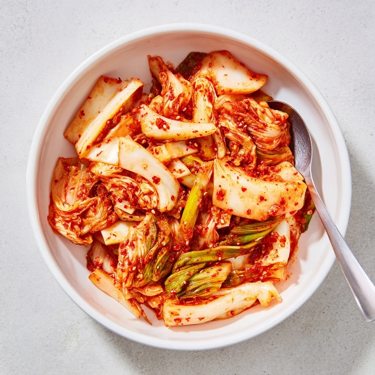 Bright red kimchi in a glass jar shows crunchy napa cabbage and daikon radish with a vibrant, tangy Korean side dish ready for fermentation.  
