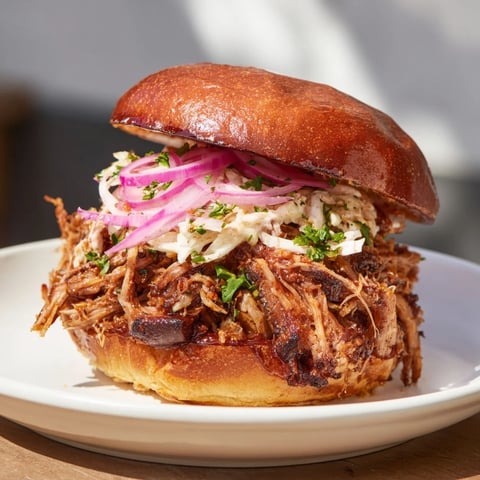 Smoke rising from fire-kissed BBQ pulled pork, piled high on toasted buns, ready to satisfy.