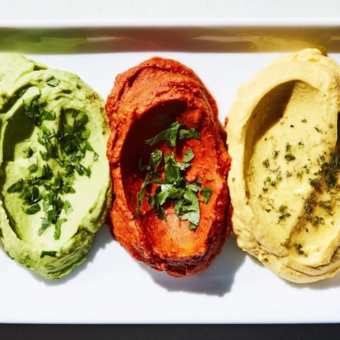 A vibrant Dip Trio featuring creamy avocado, roasted red pepper, and turmeric hummus dips in a line.