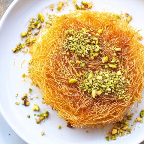 Golden, crispy Lebanese Knafeh cheese dessert with a generous drizzle of sweet syrup and pistachios.