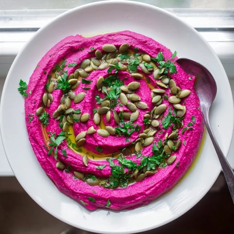 Vibrant Beet Hummus in a rustic white bowl, garnished with olive oil drizzle, toasted pumpkin seeds, and fresh parsley, ideal for dipping.