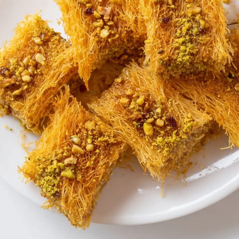 Syrupy, sweet Egyptian Konafa showing off layers of crispy kataifi pastry and chopped nuts.