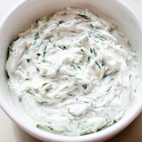 Creamy Greek Yogurt Herb Dip in a white bowl garnished with fresh dill, served with colorful vegetable crudités.  