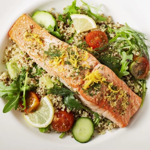 Fresh herbs and cherry tomatoes garnish a plate of warm salmon and fluffy quinoa, drizzled with lemon vinaigrette.