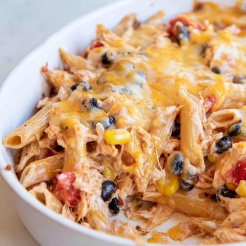 A close-up of creamy Chicken Burrito Pasta Bake, featuring penne, black beans, and shredded chicken in a rich tomato salsa.