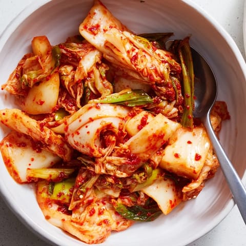 Freshly prepared spicy kimchi in a bowl features julienned carrots and scallions, showcasing the bold red chili paste and crisp texture.  