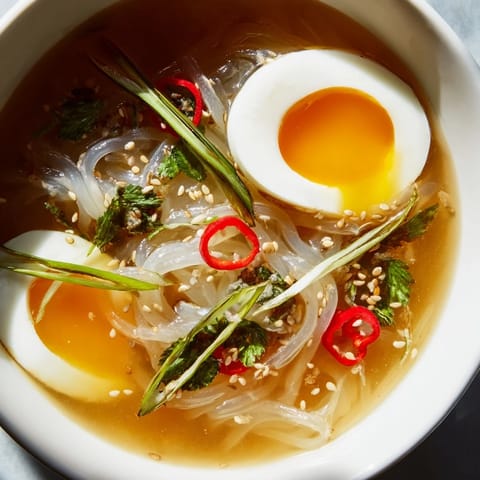 Shirataki noodles with broth served in a cozy bowl, garnished with chili slices and sesame seeds.  