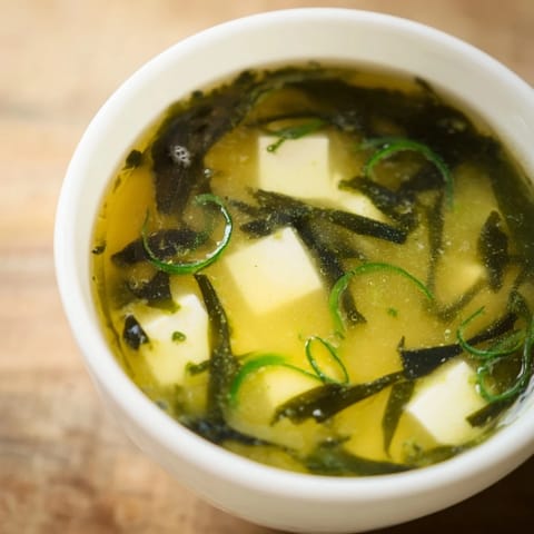 Steaming Japanese wakame soup with tender seaweed and tofu, garnished with sliced green onions for a fresh bite.
