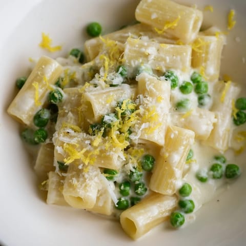 Creamy pea and lemon ricotta pasta in a white bowl garnished with fresh basil and extra Parmesan, ready to serve.  