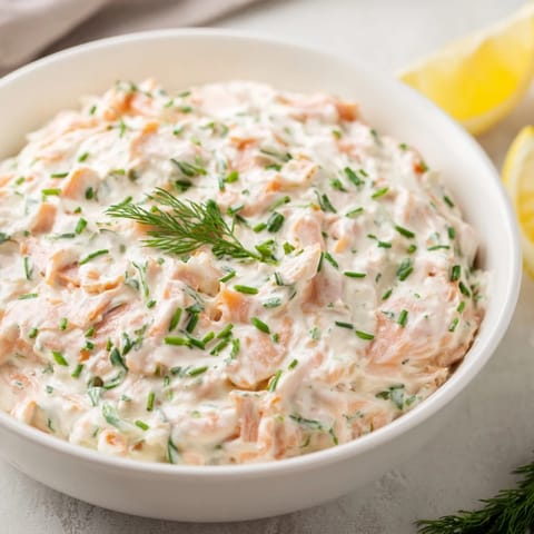 Creamy smoked salmon dip garnished with fresh dill and lemon wedges, served with crackers.  