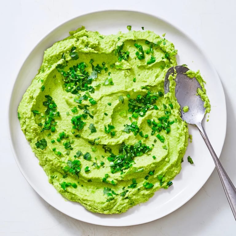 A close-up of vibrant avocado lime dip in a rustic serving bowl, surrounded by colorful vegetable sticks and fresh lime wedges.  