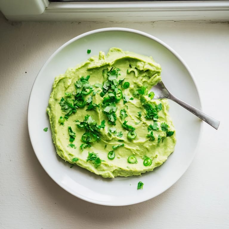 Freshly prepared avocado lime dip topped with cilantro, served alongside golden tortilla chips on a wooden board.