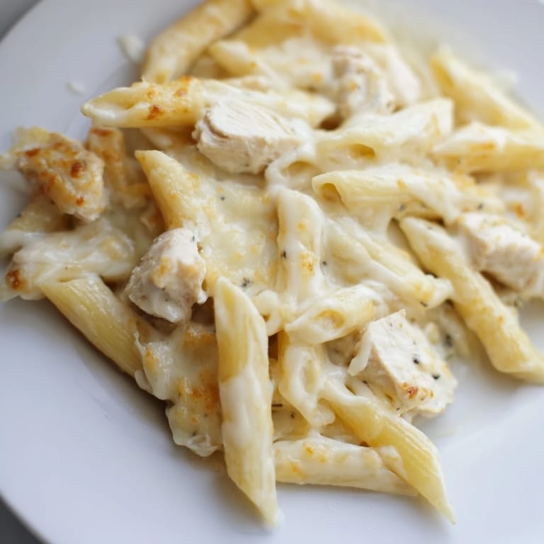 Serving spoon diving into creamy Chicken Alfredo Casserole, revealing tender pasta and diced chicken coated in rich Alfredo sauce.  